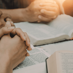 A group with clasped praying hands over Bibles